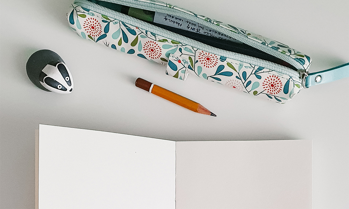 Photo of an empty sketchbook, pencil, pencil case and a small badger on a white desk.